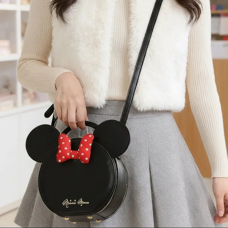 ミニーマウスのバッグを持った女性の画像です。バッグはミニーマウスの顔の形をしており、赤い水玉模様のリボンが付いています。女性は白い服を着ており、バッグは肩からかけています。