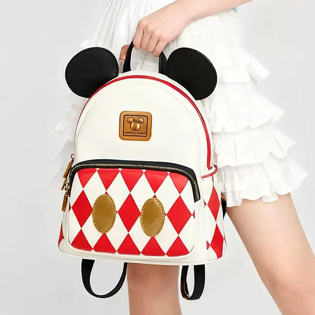 ミッキーマウスの耳が付いたリュックサック。白と赤の菱形模様で、前面にはミッキーマウスの顔がデザインされています。女性が手に持っています。