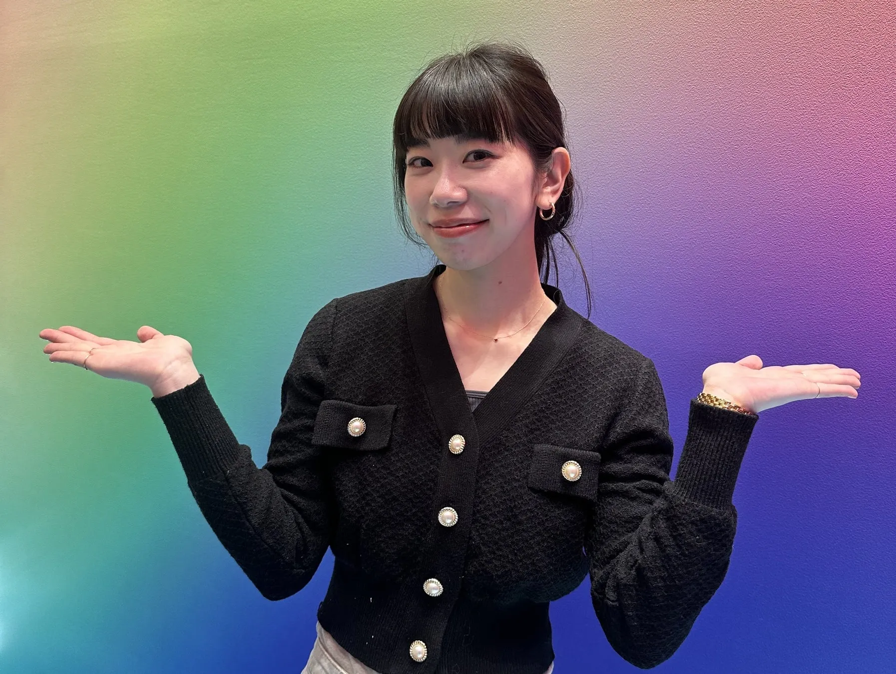 女性が両手を広げて笑顔を見せる写真。背景は虹色。