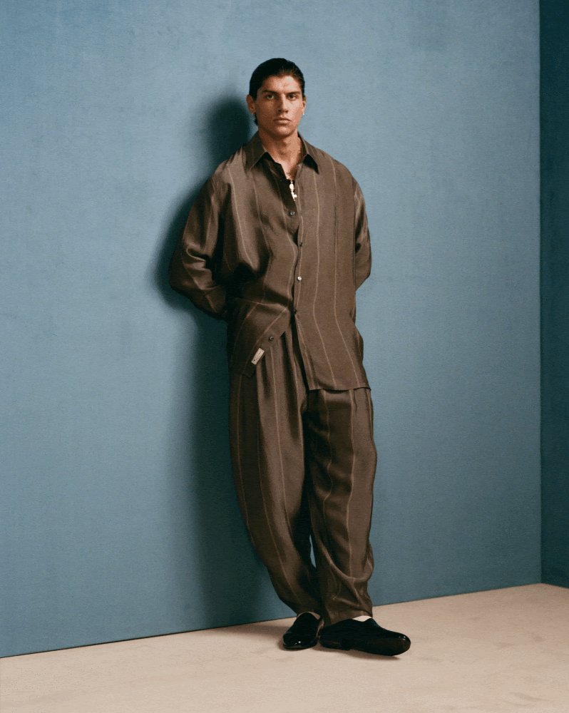 茶色のストライプのシャツとパンツのスーツを着ており、黒い靴を履いている男性