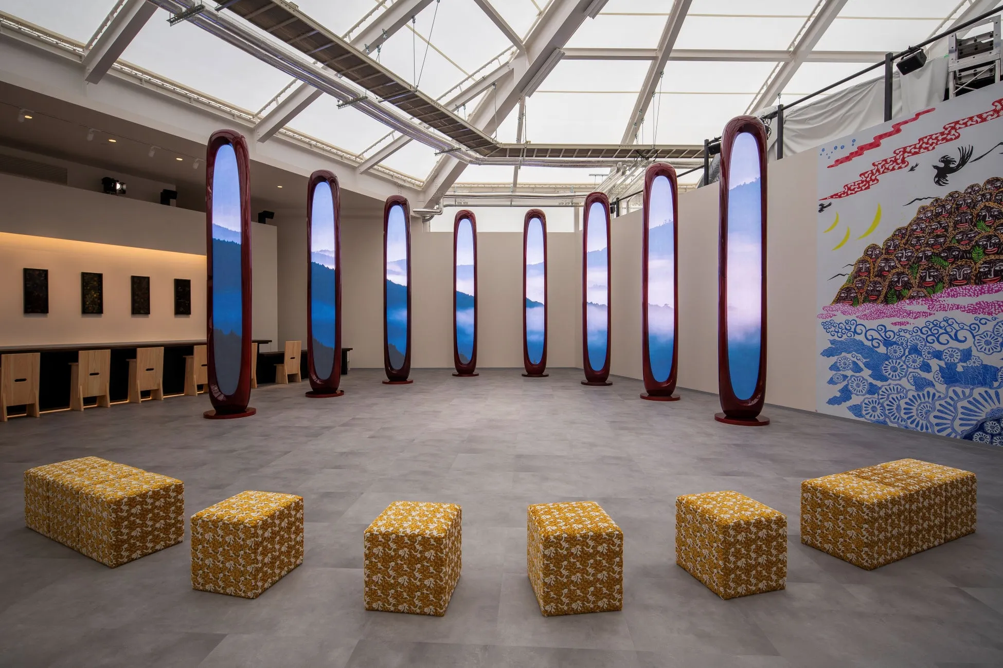 展示会場の様子。円状に配置された縦長のディスプレイには風景が映し出され、その周りにはクッションが置かれている。
