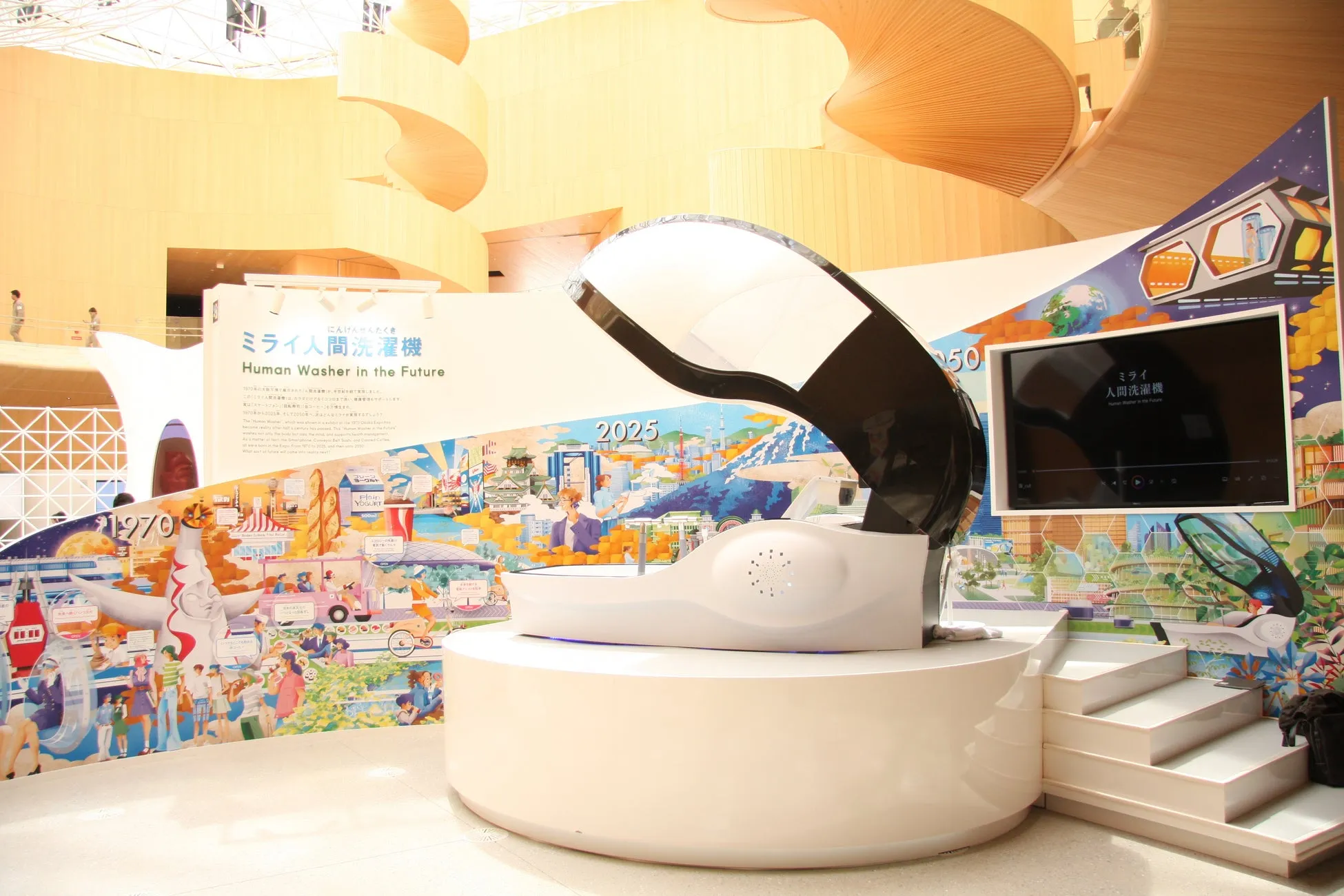 未来の人間洗濯機を紹介する展示。展示空間には、未来のビジョンを描いたイラストや、1970年代から2025年までの年表が示されている。