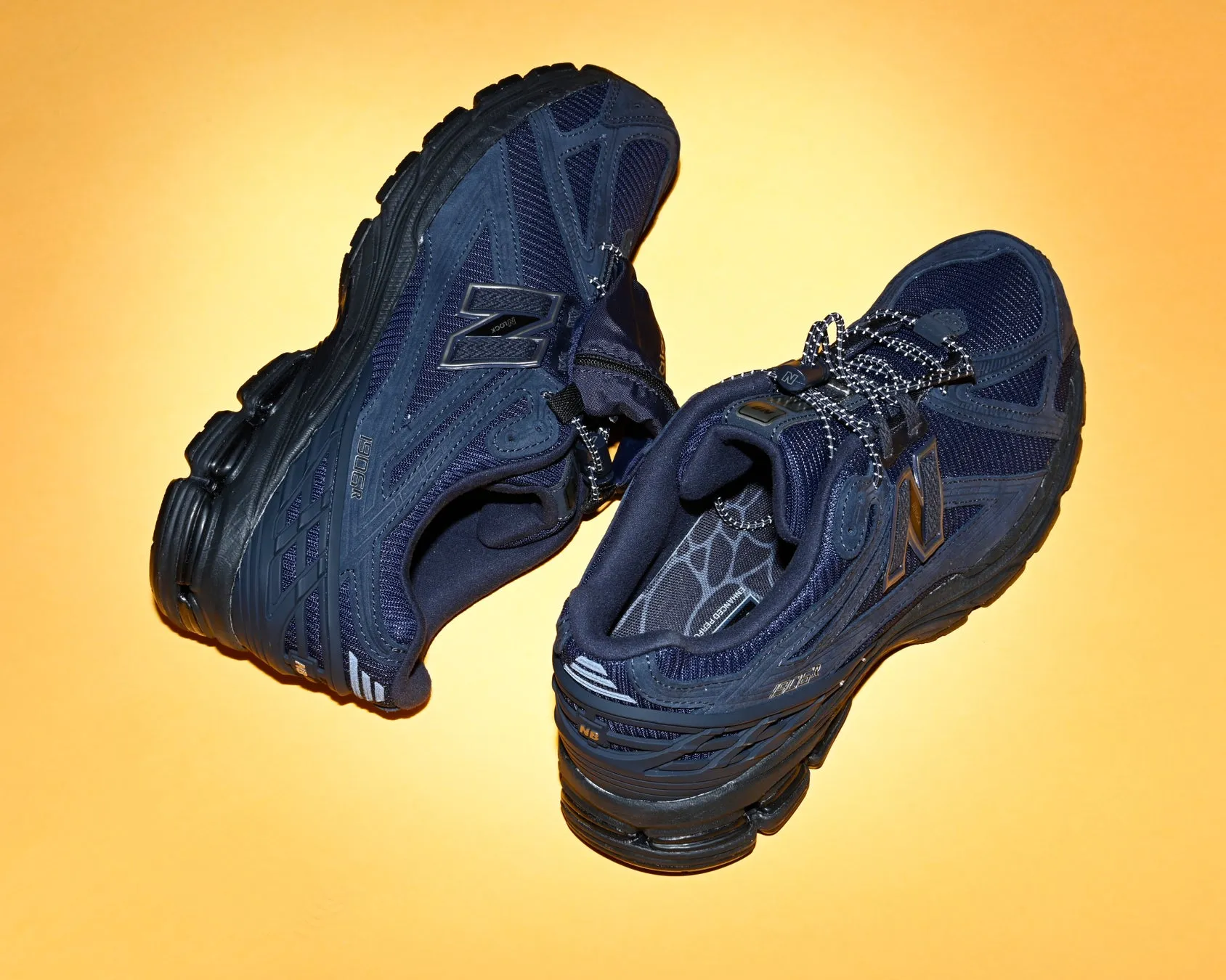 紺色の New Balance のスニーカーのペアが、黄色の背景に置かれています。