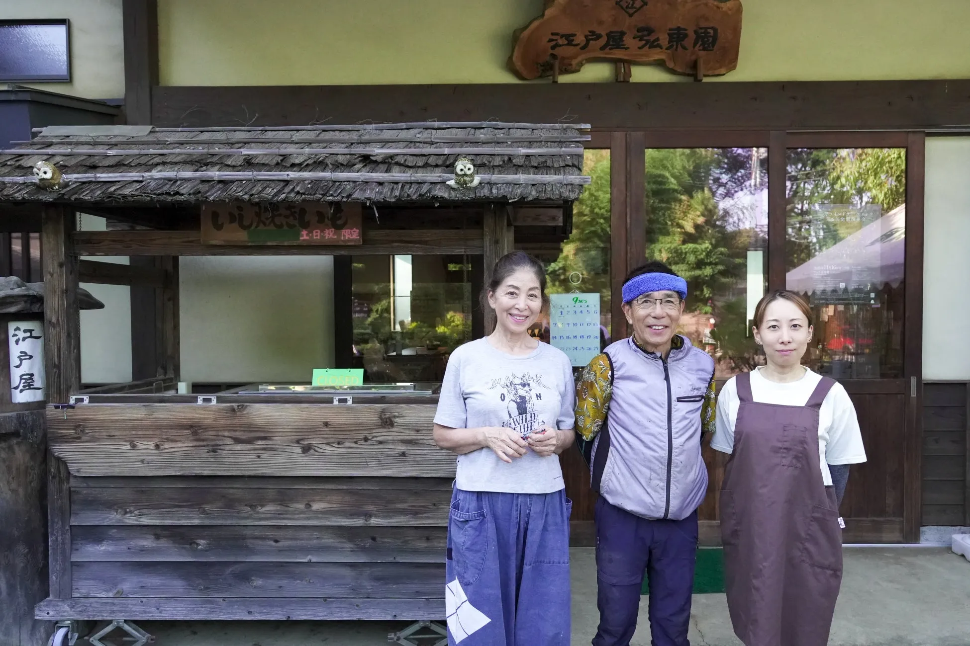 お店の前で笑顔で立っている3人の人々の写真です。