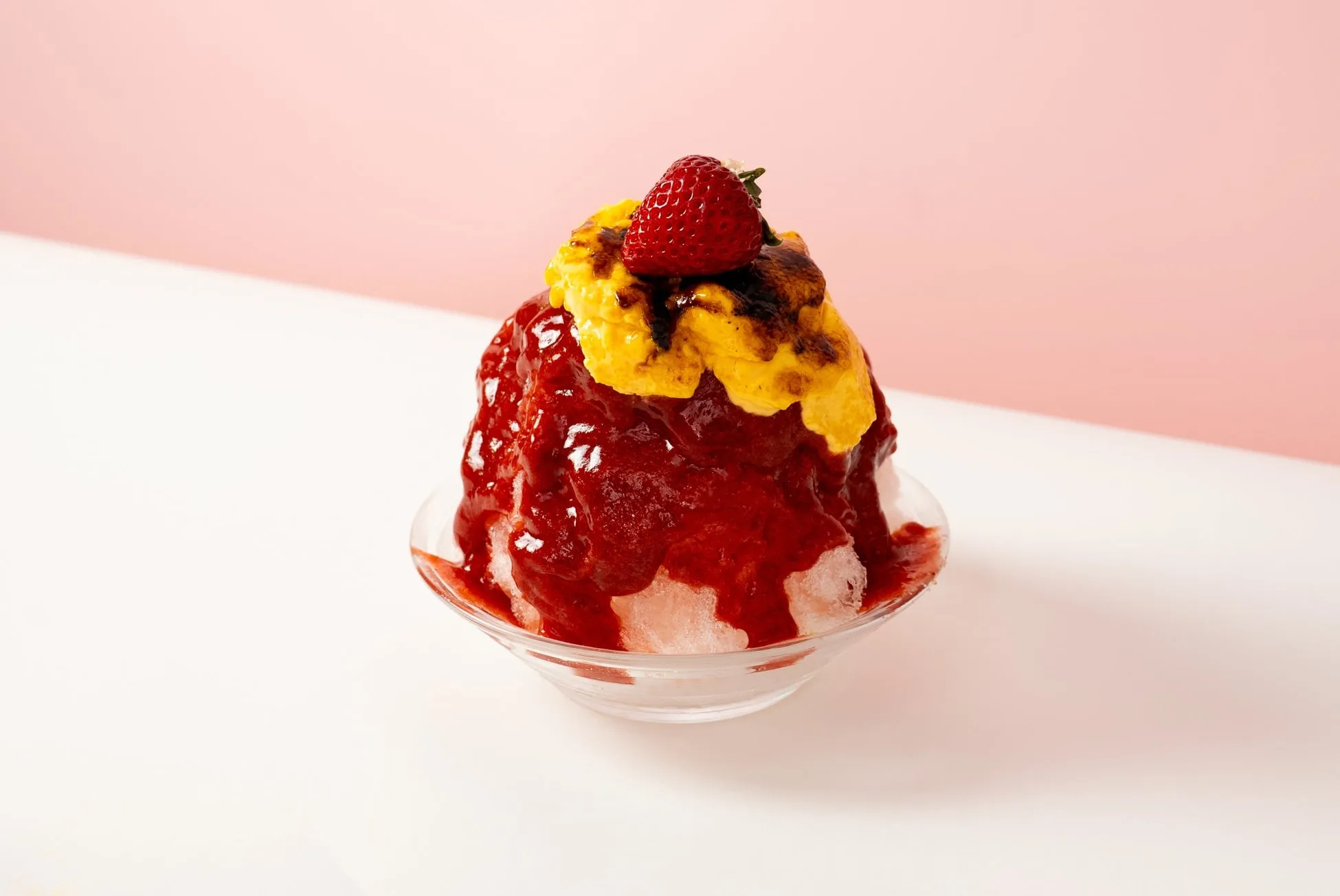 いちごがトッピングされたかき氷の写真です。かき氷は赤色のソースで覆われ、黄色いクリームと焦げたソースがトッピングされています。