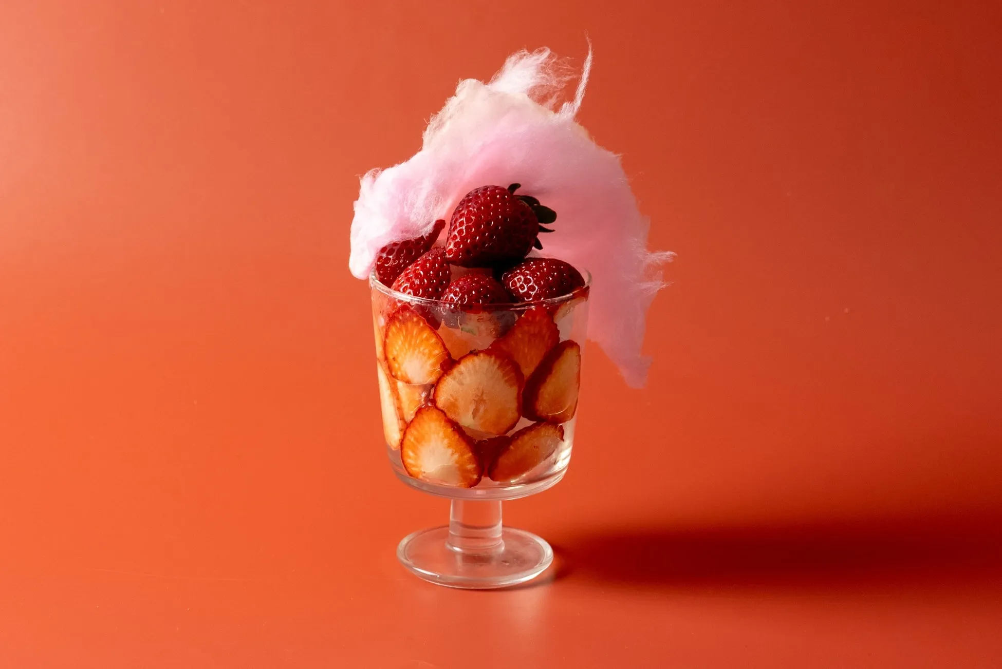 グラスに入ったイチゴと綿菓子のデザート。背景はオレンジ色。