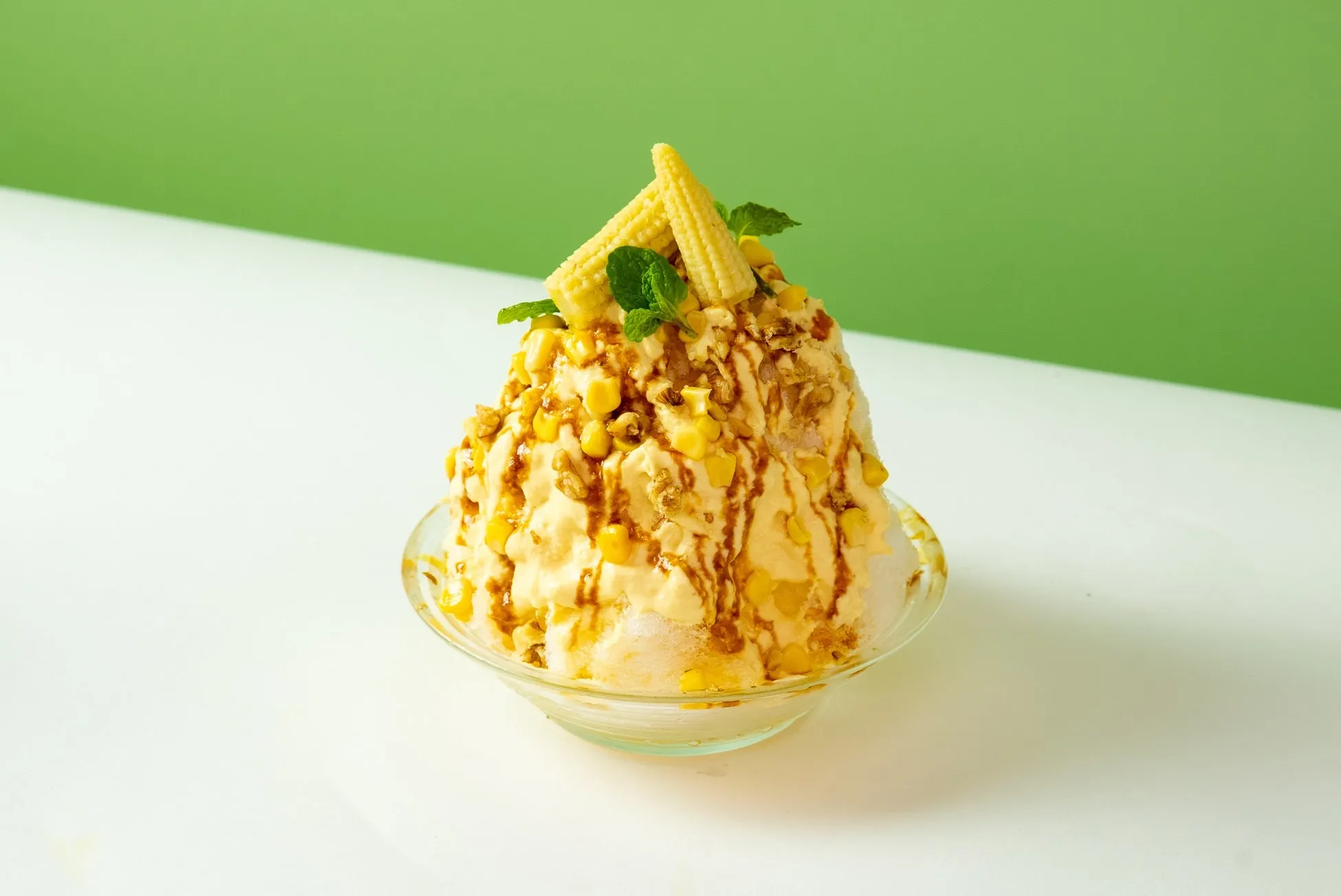トウモロコシとミントで飾られた、ガラスのボウルに入ったかき氷のクローズアップ写真。