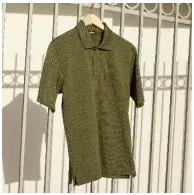 オリーブ色のポロシャツが、白い壁の前に掛けられている様子。