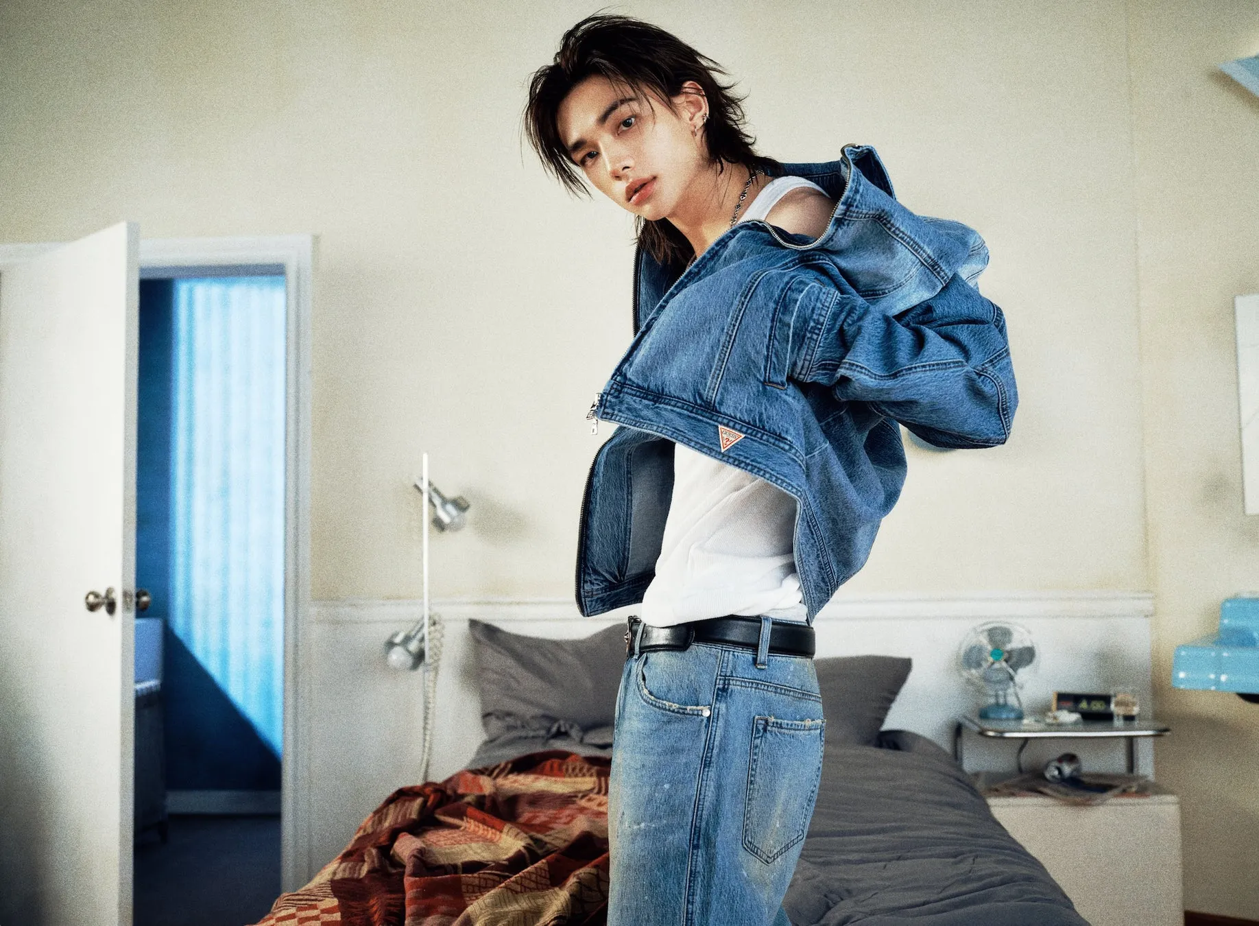 デニムジャケットを着た男性が、ベッドルームでポーズをとっています。