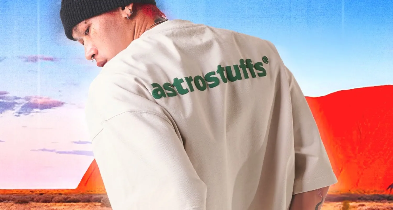 男性が背中を向けている写真で、ベージュのシャツを着ており、背中には「astrostuffs®」と緑色で書かれています。背景には空と赤い岩のような風景があります。
