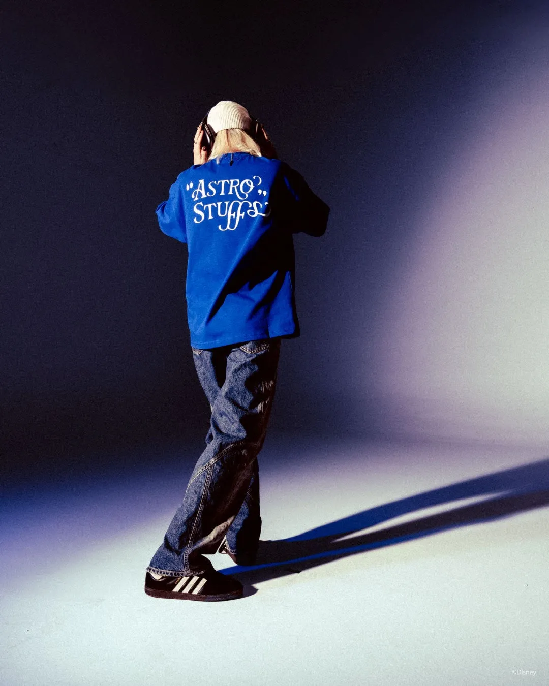 青い服を着た人物がヘッドホンをして立っている写真。背中には白い文字で"ASTRO? STUFFS"と書かれている。ジーンズと黒い靴を履いている。