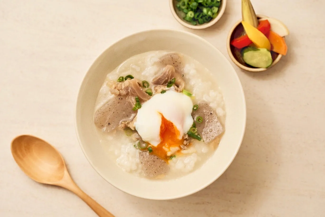 ご飯の上に温泉卵、肉、ネギが乗った料理の写真。副菜として漬物とネギも添えられている。