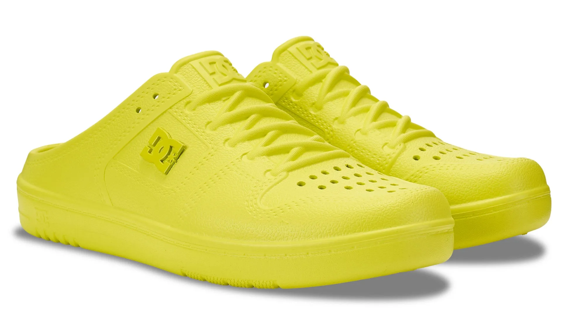 鮮やかな黄色のDCブランドのスリッポンシューズのクローズアップ写真。シューズは革新的なデザインで、レースと穴のディテールが施されています。DCロゴがサイドに表示されています。