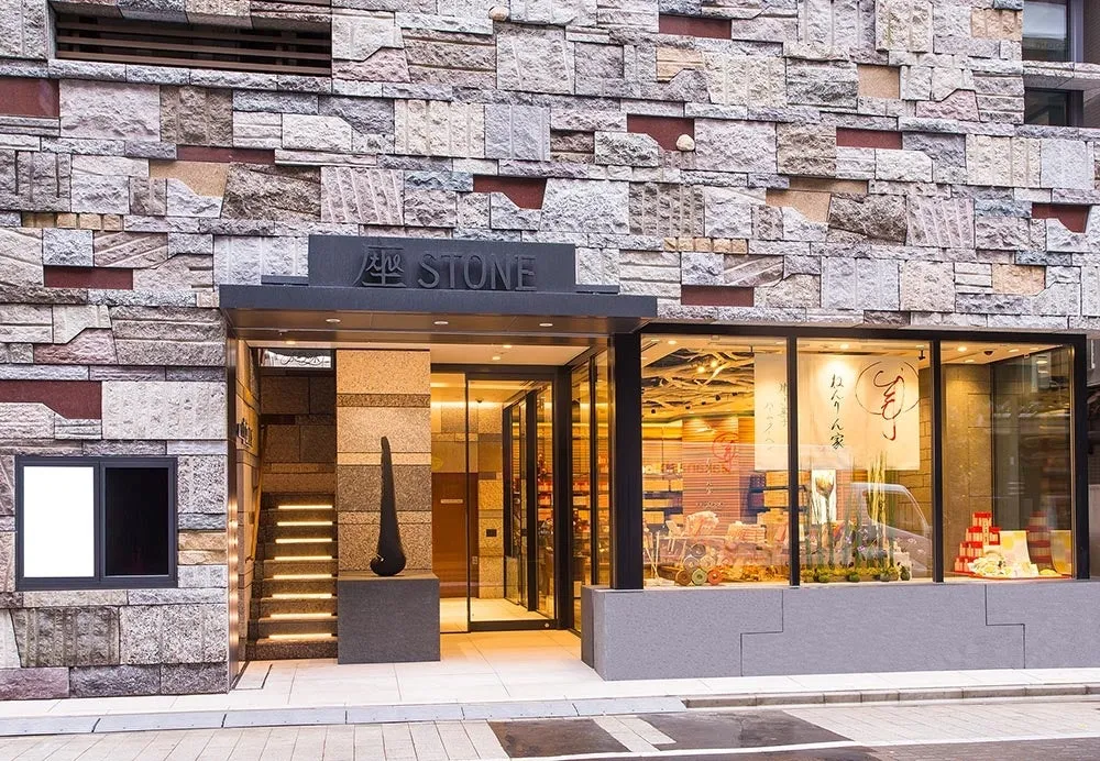 石壁に覆われた建物の入り口の様子です。入り口の上には「座 STONE」と書かれた看板があり、ガラス張りのショーウィンドウには商品が並んでいます。お店の名前は「ねんりん家」のようです。