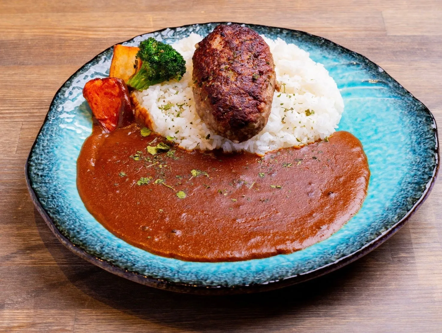 カレーライス、ハンバーグ、ご飯、ブロッコリー、トマト、ジャガイモが盛られた料理の写真です。