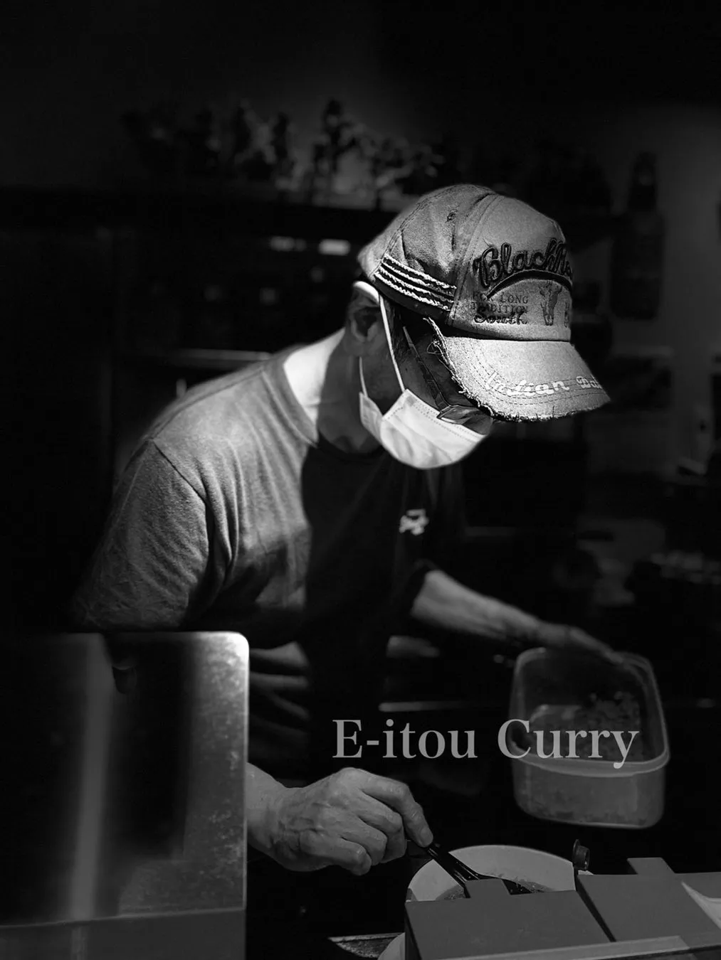 店内で調理をする店員。マスクと帽子を着用し、カレーを盛り付けている様子。