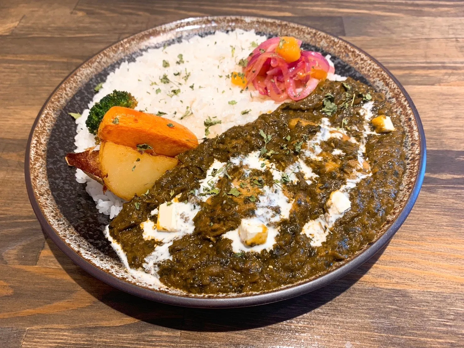 カレーライス。ほうれん草ベースのカレーに、ライス、野菜、チーズが添えられています。