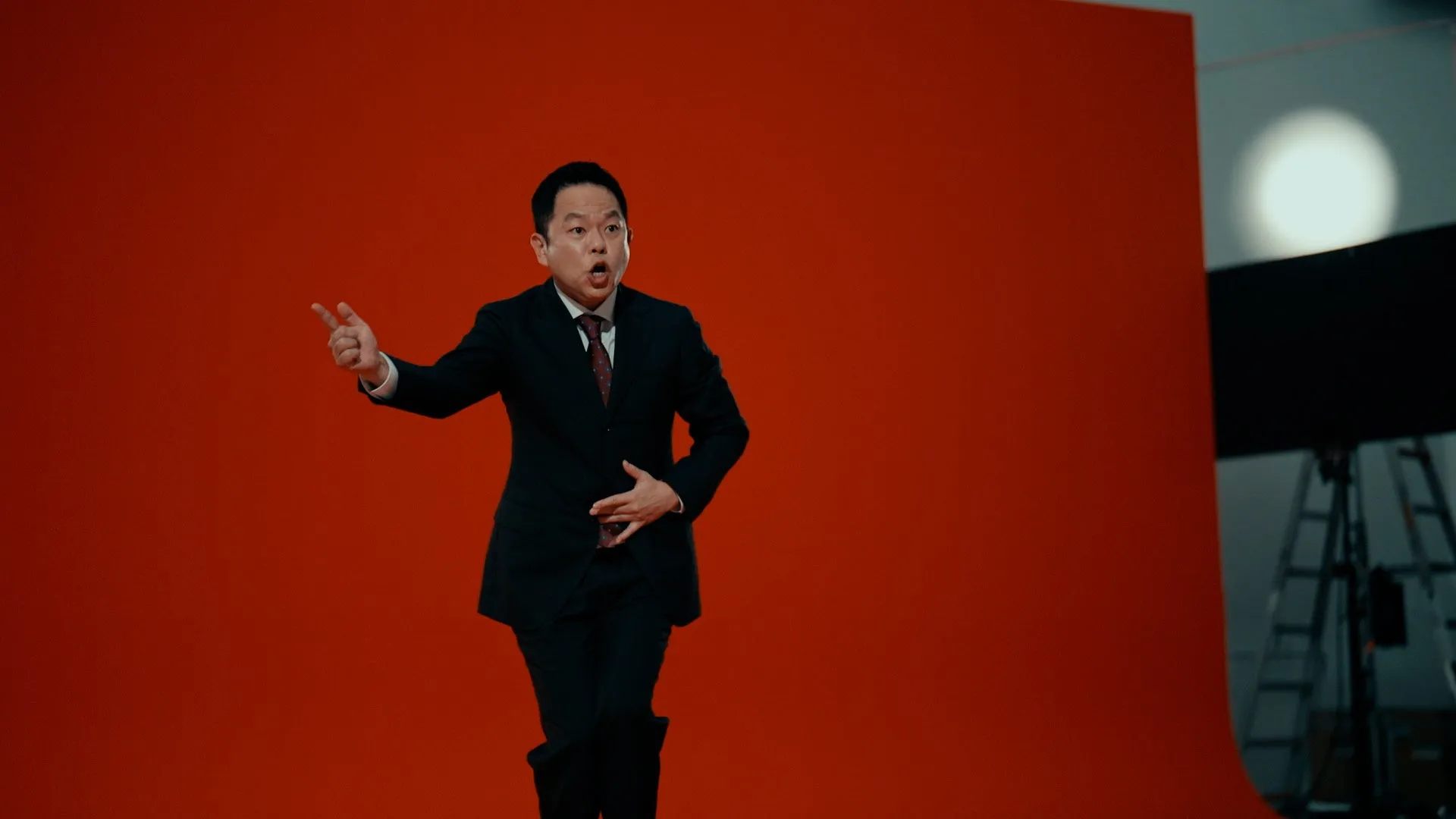 赤い背景の前で、スーツを着た男性が驚いた表情でポーズをとっている様子を捉えた写真です。