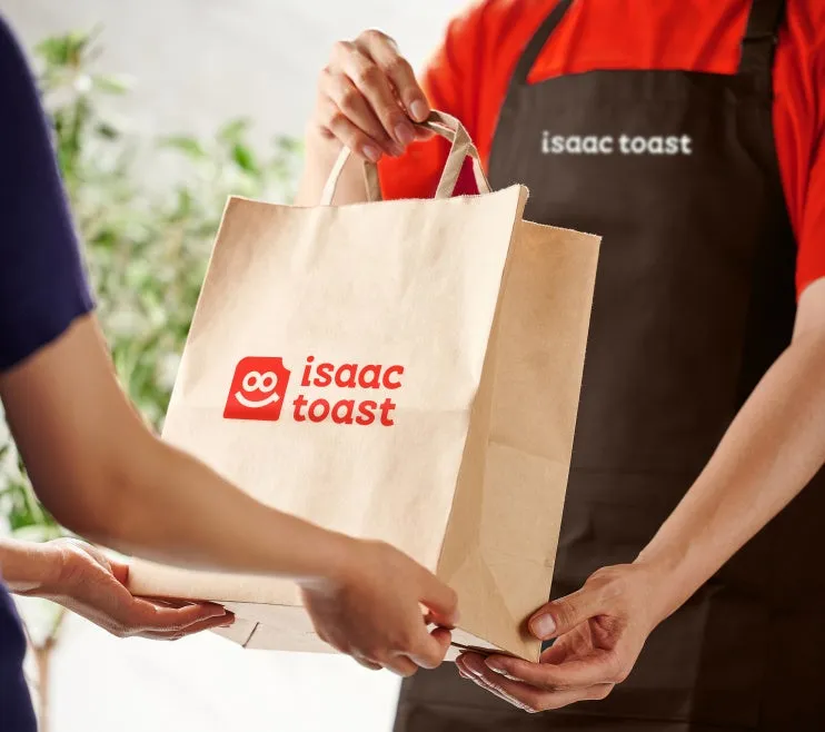 お店の店員が、顧客にテイクアウト用の紙袋を手渡している様子が写っています。