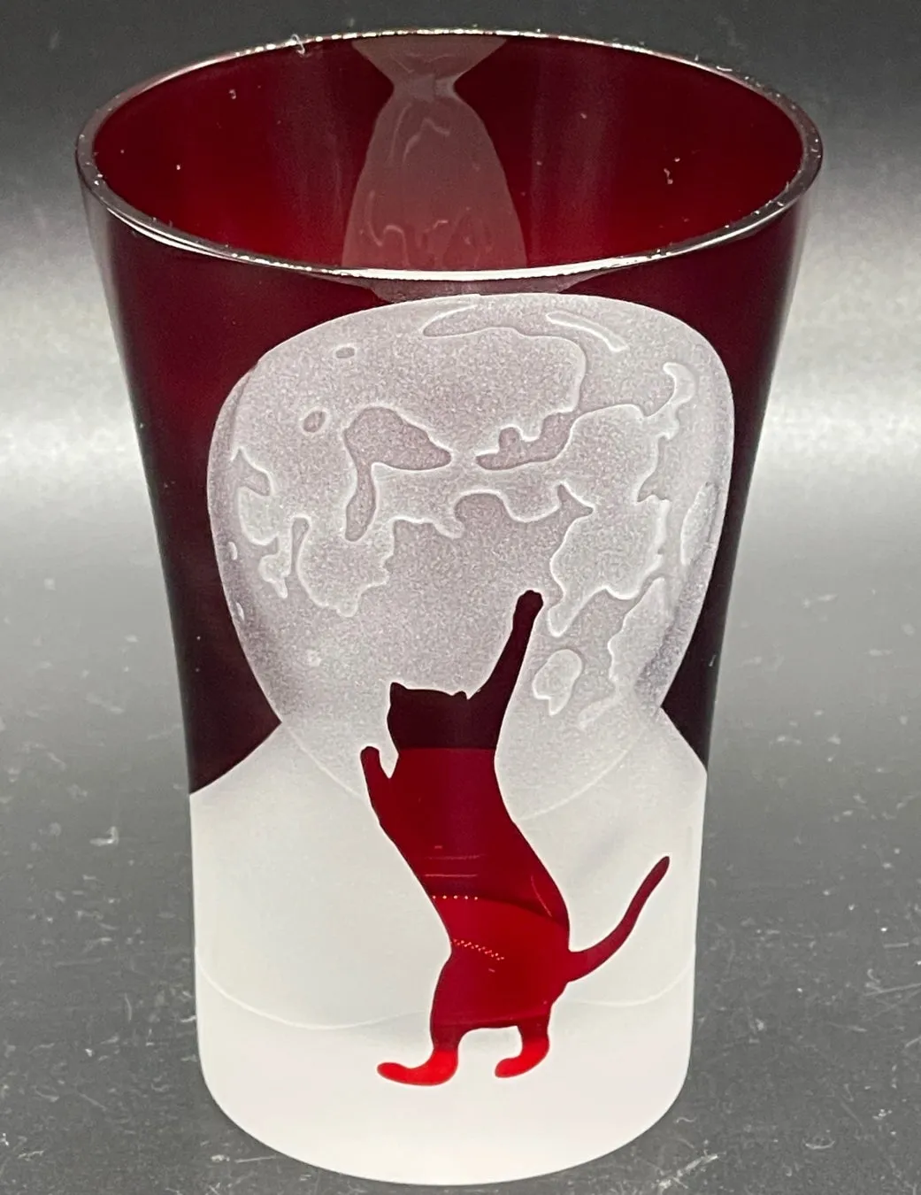 赤いグラスに猫と月が描かれたデザイン。グラスは赤色で、猫が月に向かって手を伸ばしている様子が描かれています。