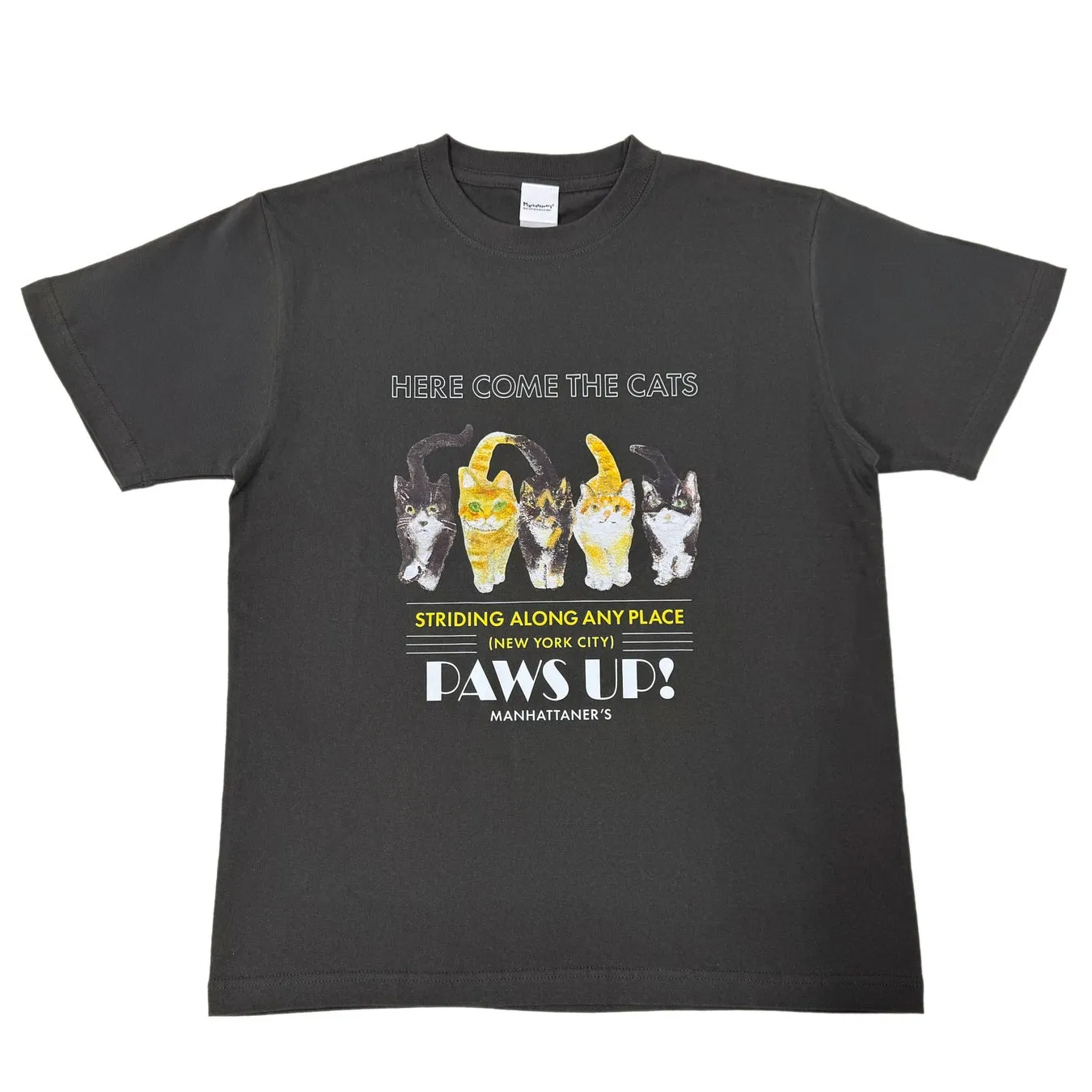 黒いTシャツに猫のイラストと文字がプリントされた画像です。「HERE COME THE CATS」の文字が上部にあり、猫が並んで歩いている様子が描かれています。「STRIDING ALONG ANY PLACE (NEW YORK CITY) PAWS UP!」の文字が下にあります。