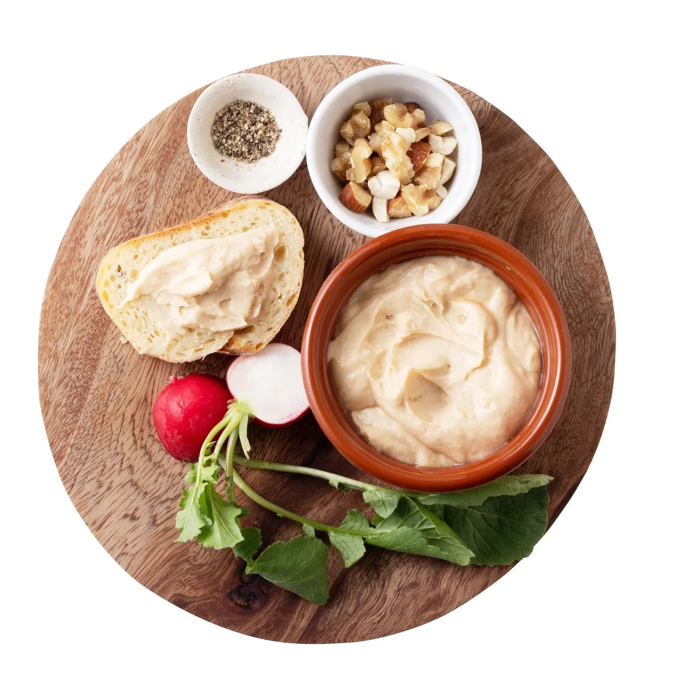 木製の円盤の上に、パン、ディップ、ナッツ、ラディッシュ、スパイスが置かれている写真です。