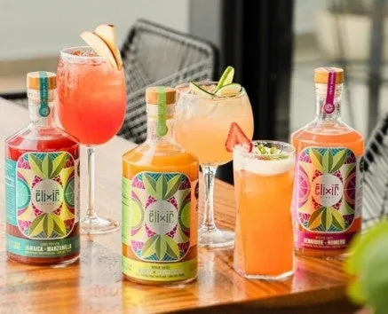 テーブルに並んだ、フルーツとハーブで飾られたカクテルと、elixirブランドのボトルが写った写真。