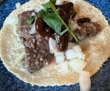 トルティーヤの上に、肉、玉ねぎ、パクチー、ソースが乗った料理の写真。