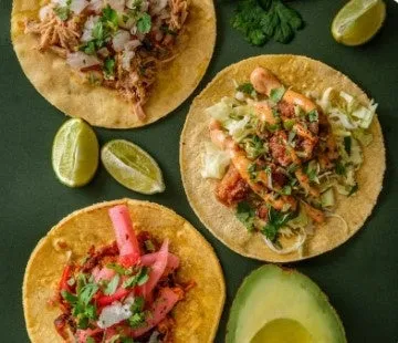 様々な種類のタコスが並んだ写真。鶏肉やエビ、アボカド、ライムなどが添えられている。