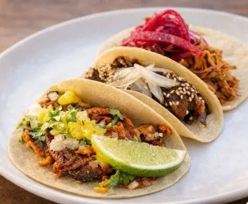 3つのタコスが白い皿に盛り付けられた写真。それぞれ異なる具材が使われており、美味しそうに見える。