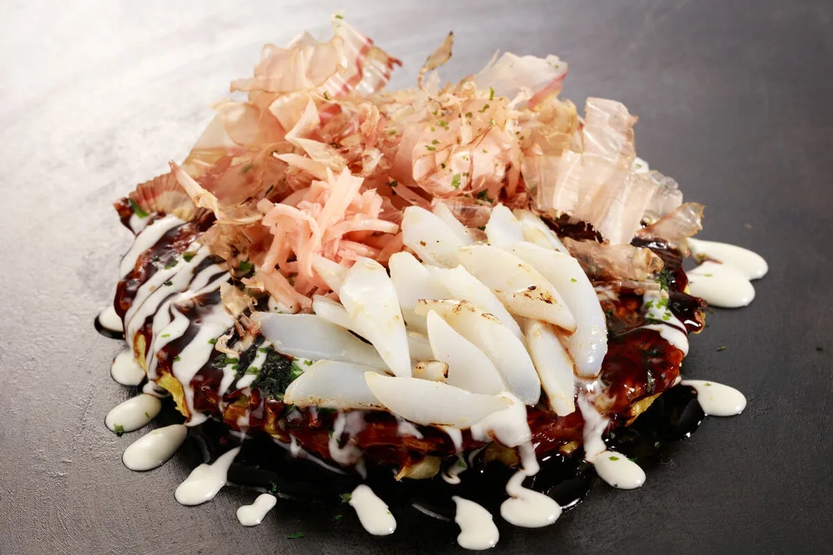 お好み焼きのクローズアップ写真。鰹節、紅しょうが、イカがトッピングされている。