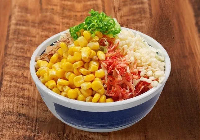 様々な食材が盛られた丼のクローズアップ写真。コーン、ネギ、揚げ玉、桜エビ、ご飯など。