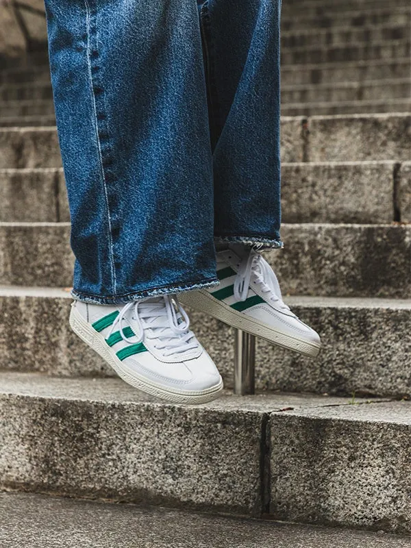 階段に座って足元を映した写真。白いスニーカーにグリーンのラインが入っており、ジーンズを履いている。