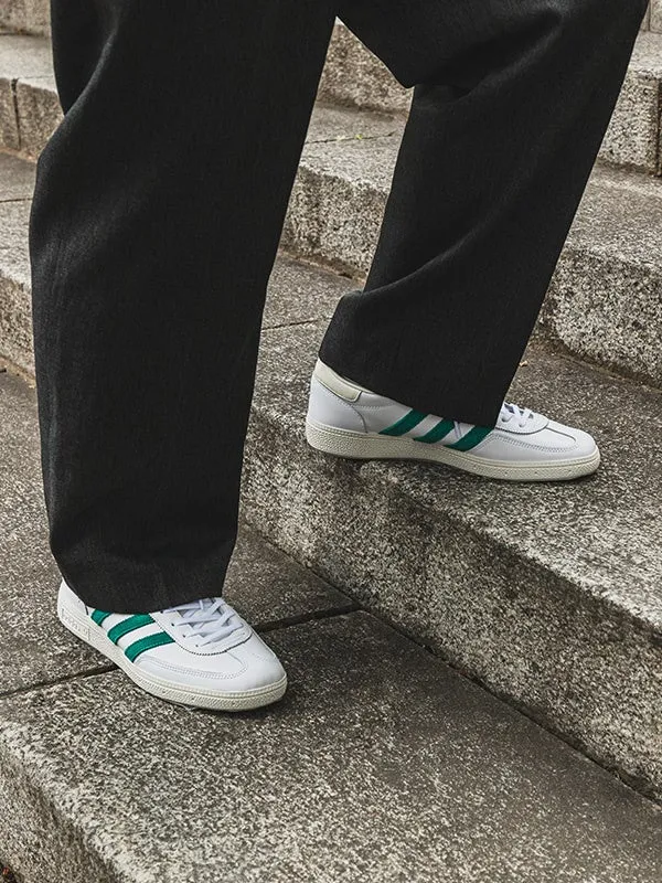 階段を上る人の足元を捉えた写真。白いスニーカーに緑色のラインが入っており、黒いズボンと組み合わされている。