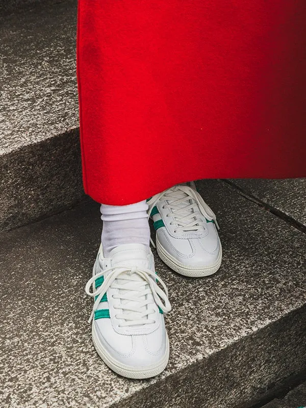 白いスニーカーと赤い服を着た人の足元を捉えた写真です。スニーカーは、白い革素材に緑色のラインが入っており、白い靴紐が特徴です。足元は階段の上にあり、赤い服は足元を覆うように写っています。