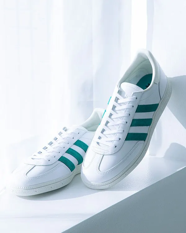 白いスニーカーのペアが、白い背景に置かれています。スニーカーには緑のストライプが入っています。