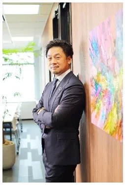 腕組みをして壁に寄りかかるスーツ姿の男性の写真