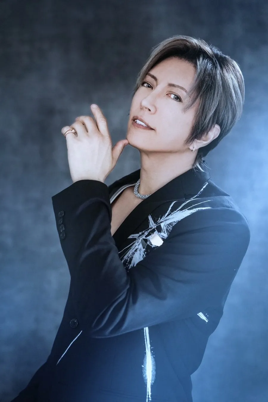 黒いジャケットを着た男性のポートレート。彼は指で顎に触れ、カメラを見ている。