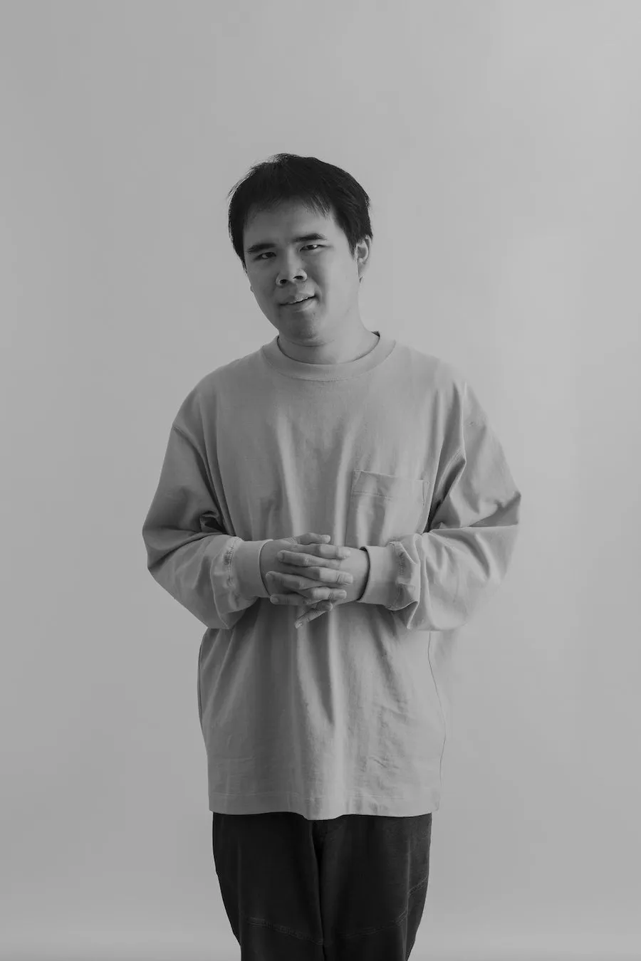 正面を向いて微笑んでいるアジア系の男性のモノクロポートレート。