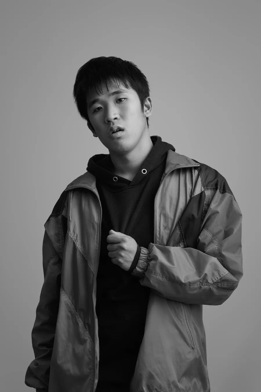 モノクロのポートレート。男性がカメラ目線で、黒いパーカーとジャケットを着ている。