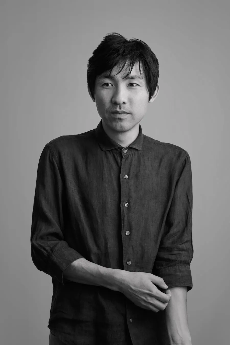 モノクロのポートレート写真。東洋系の男性が正面を向き、やや困った表情で写っている。