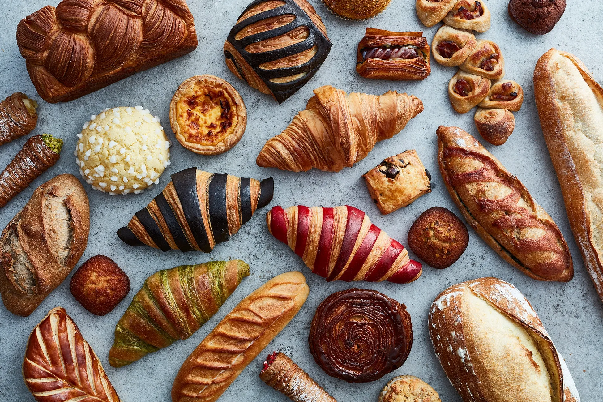 様々な種類のパンが並べられた写真。クロワッサン、デニッシュ、バゲットなど、様々な種類のパンがテーブルに配置されている。