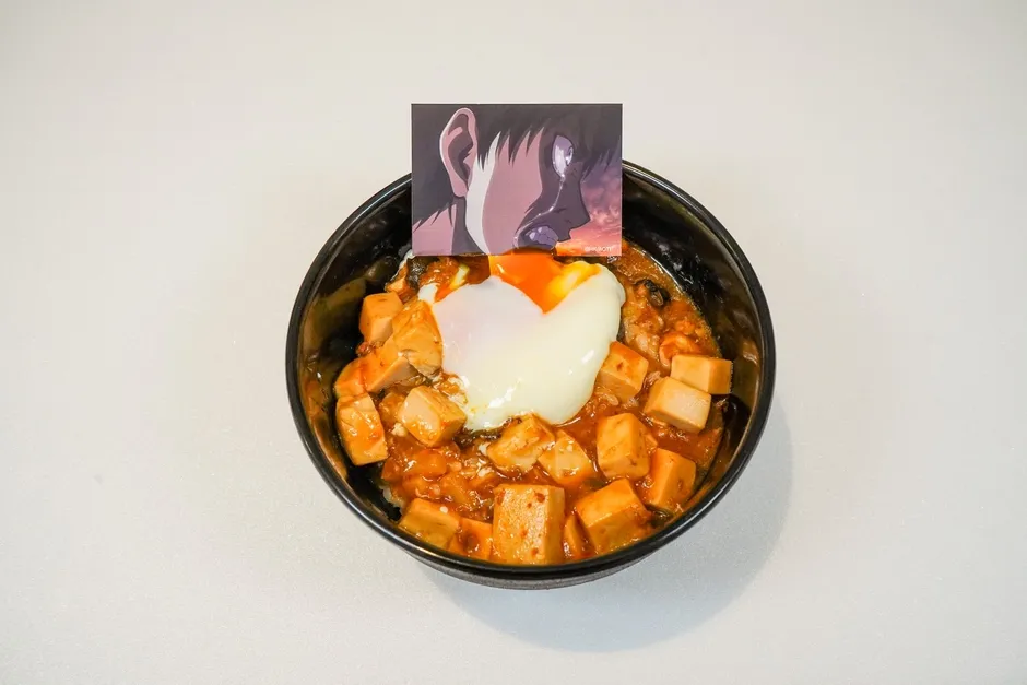 麻婆豆腐丼の上に温泉卵が乗っており、アニメのキャラクターが描かれたカードが添えられている。