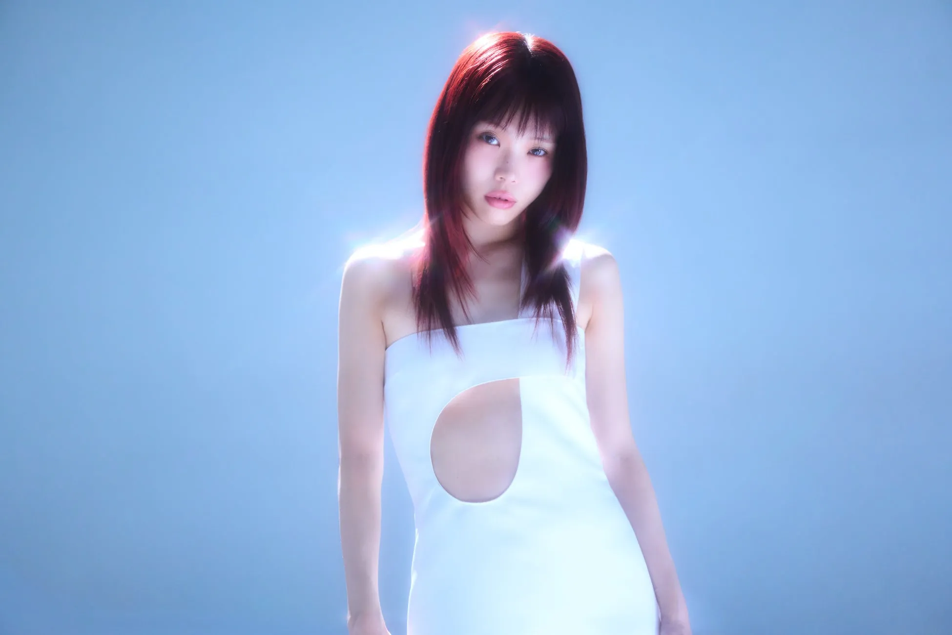 白いワンピースを着た女性のポートレート。女性は赤い髪で、カメラを見つめています。背景は青色です。