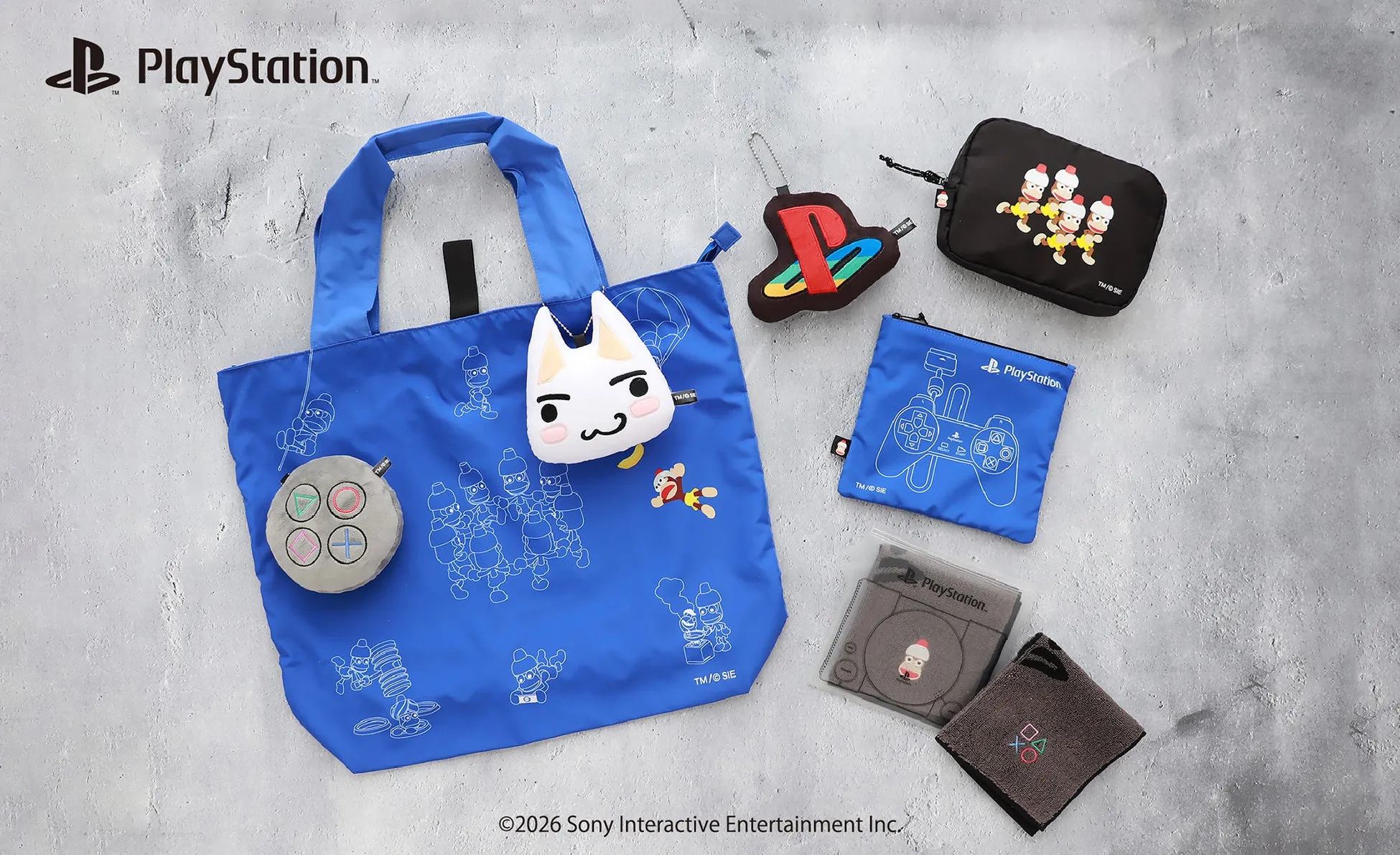 PlayStation関連のグッズが写った写真。青色のトートバッグ、ポーチ、キーホルダー、タオルなど様々なアイテムが写っている。