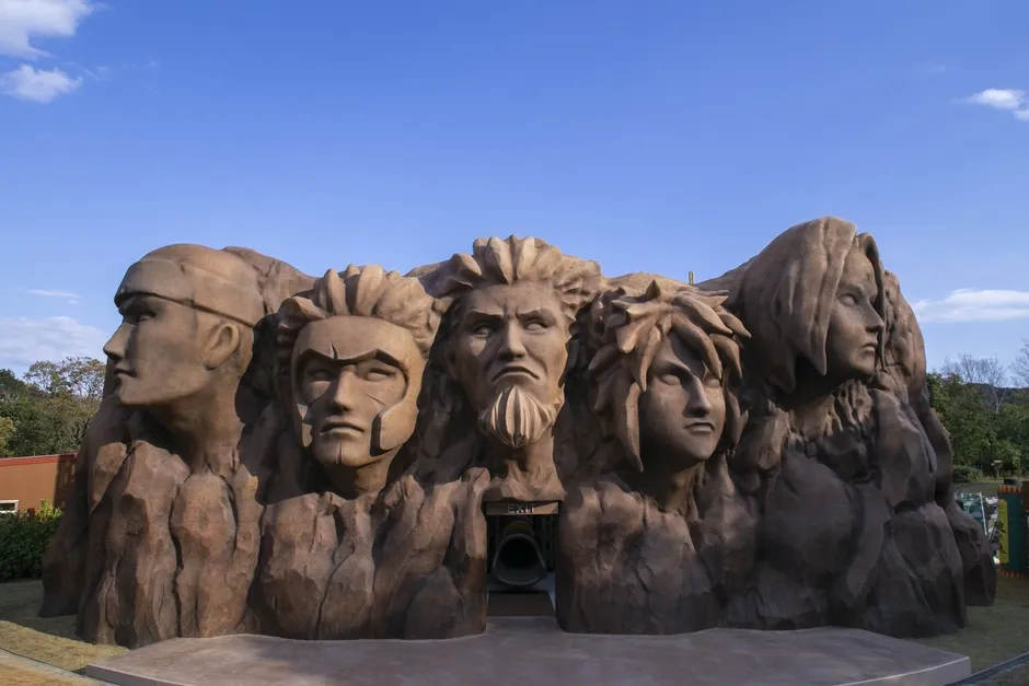 巨大な岩に彫られた像。NARUTOのキャラクターの顔が彫られている。青い空の下に立っている。