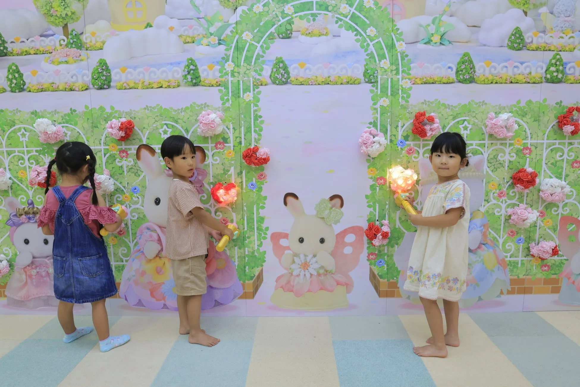 子供たちが、花やウサギの絵が描かれた背景の前で、光るおもちゃを持っている写真です。