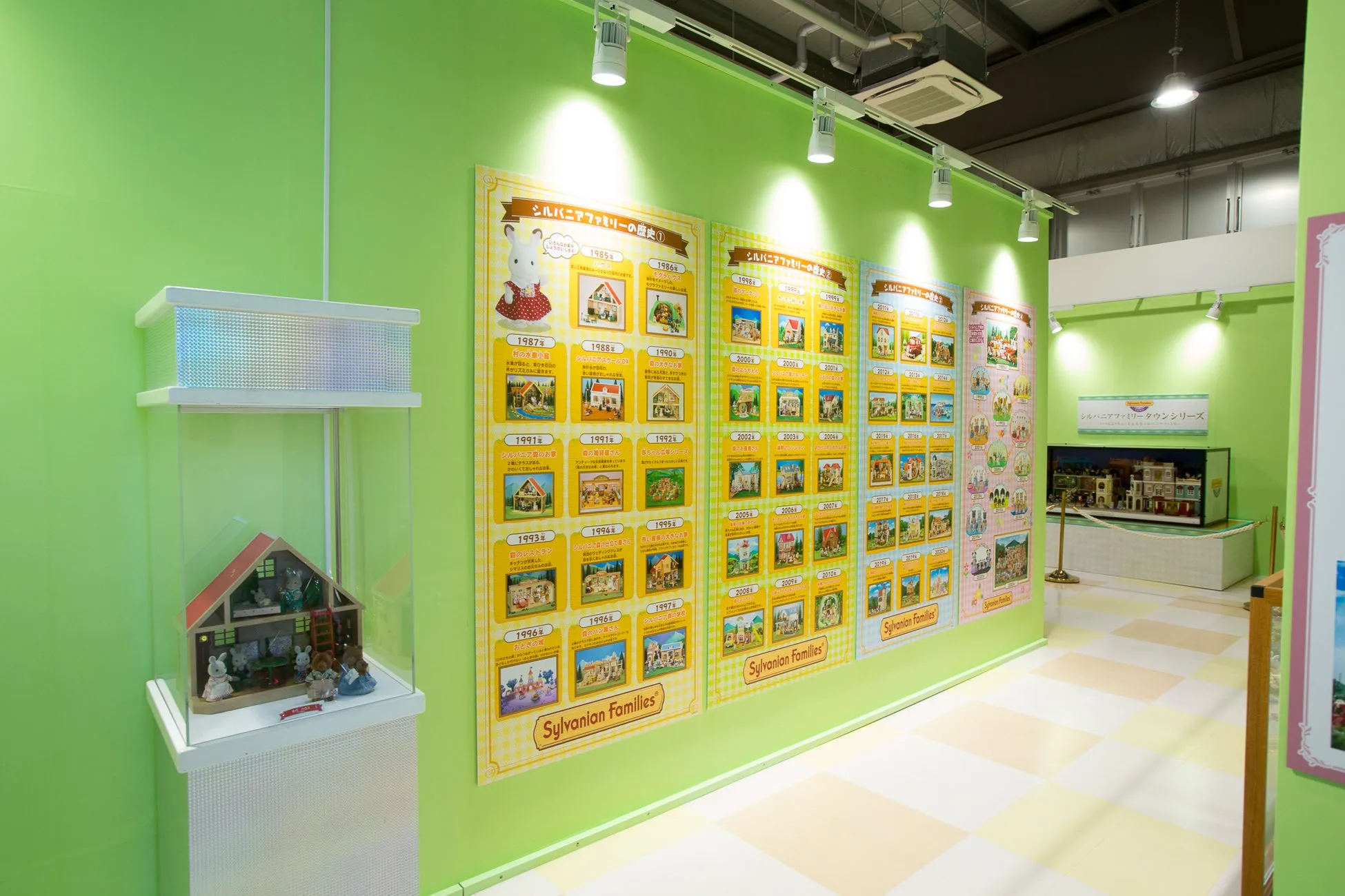 シルバニアファミリーの展示。壁にはシルバニアファミリーの歴史が年表形式で展示され、ショーケースにはシルバニアファミリーの家や人形が飾られています。展示室は緑色を基調としています。