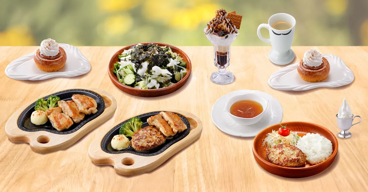 様々な料理が並んだ写真。ハンバーグ、チキンステーキ、サラダ、デザートなど、様々な料理が木製のテーブルに配置されている。全体的に明るく、美味しそうな印象を与える。