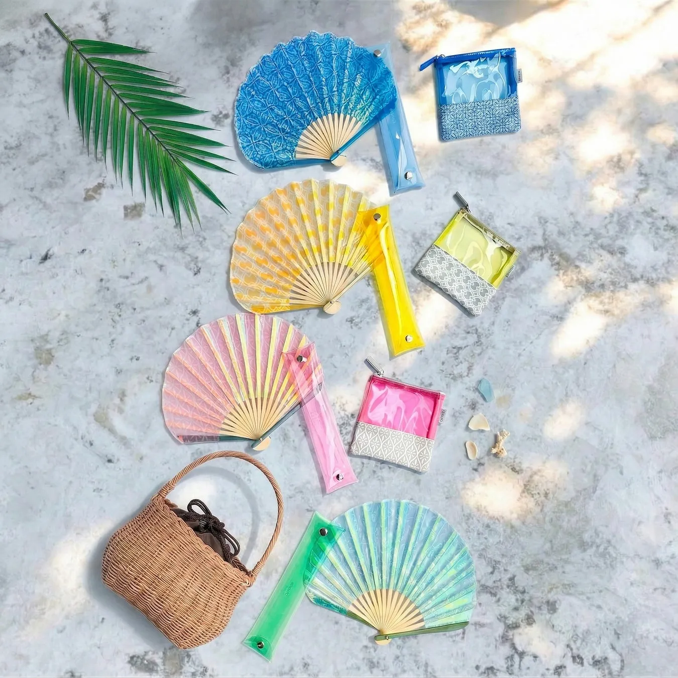 扇子、ポーチ、カゴバッグなどが配置された画像。カラフルな扇子と透明なポーチが夏らしい雰囲気を醸し出している。カゴバッグも添えられ、ビーチや夏のイベントを連想させる。